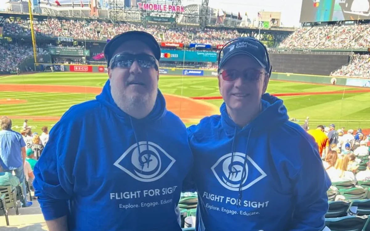 Brian and Ed at the 2023 MLB All-Star game in Seattle, both wearing blue hoodies with the Blind Travel Foundation logo in white, the field behind them.