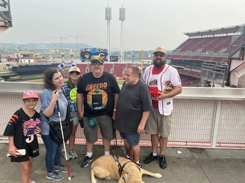 Six people standing together at Great American Ball Park, with Brian's guide dog Wesley on the ground.