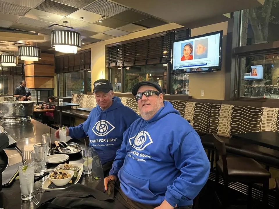 Ed and Brian at a bar in their royal blue Blind Travel Foundation sweatshirts.
