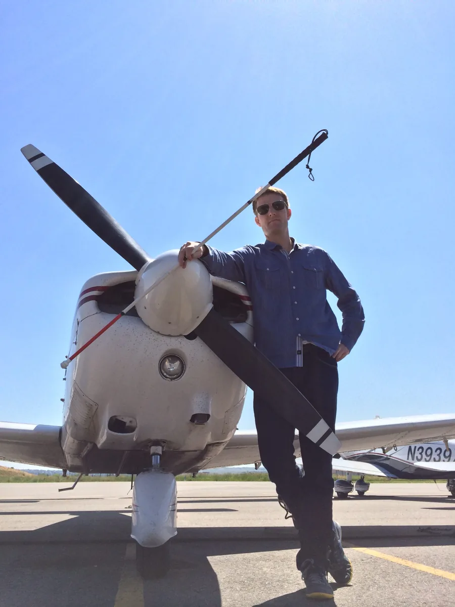 A traveller standing beside a small propeller aircraft on a sunlit runway, 2014.