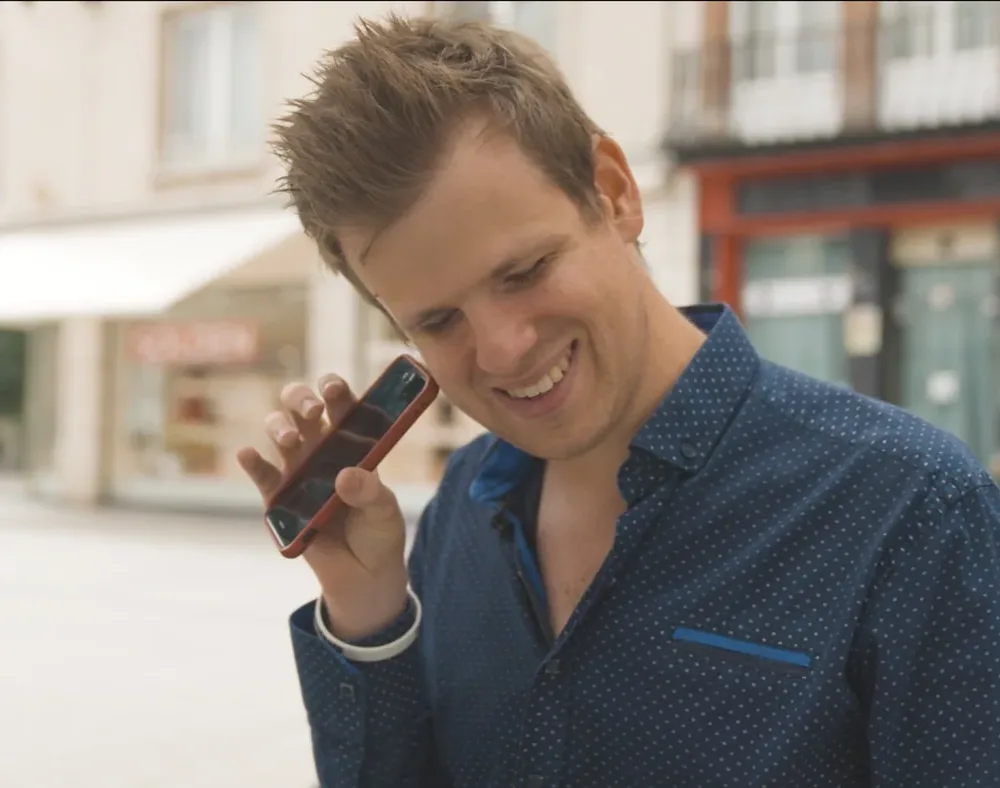 Anthony Reyers smiling, holding a phone to his ear on a city street.