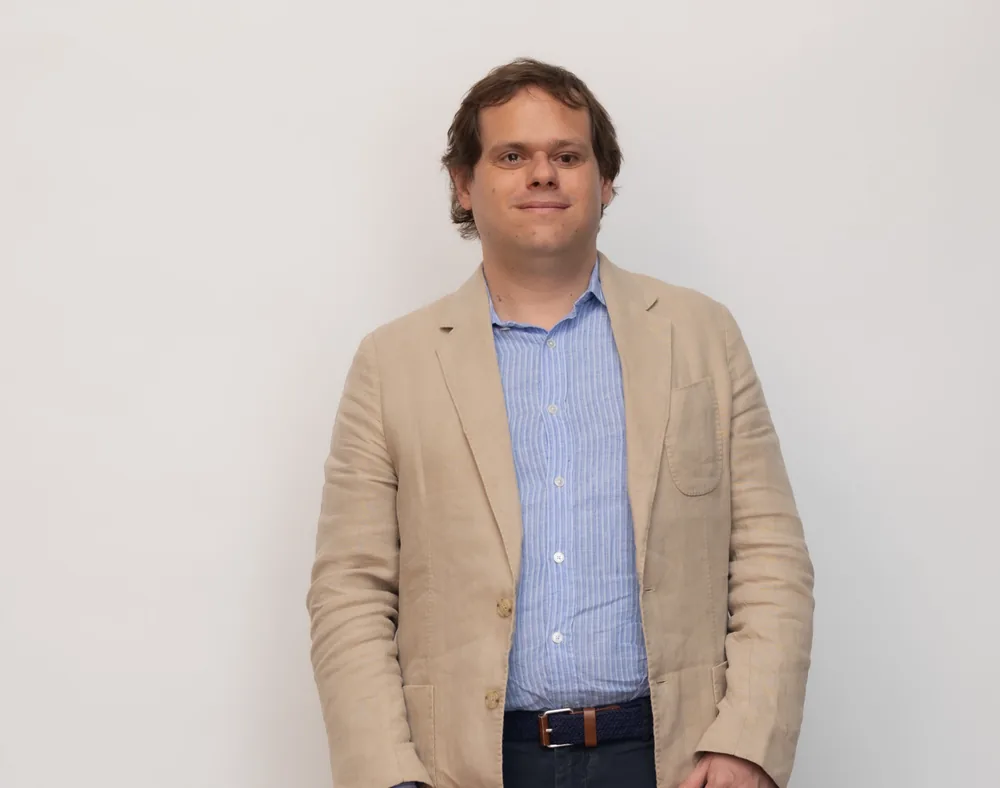 Ignasi Cambra standing against a plain studio wall in a tan linen jacket.